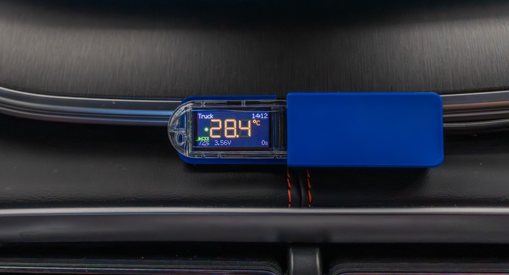 Close-up of the blue °Celsi mini-hub mounted on a vehicle dashboard, its display reading Truck 28.4°C at 14:12